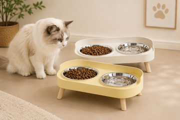 Cat sitting next to a yellow pet feeder with two bowls of food on a beige floor.